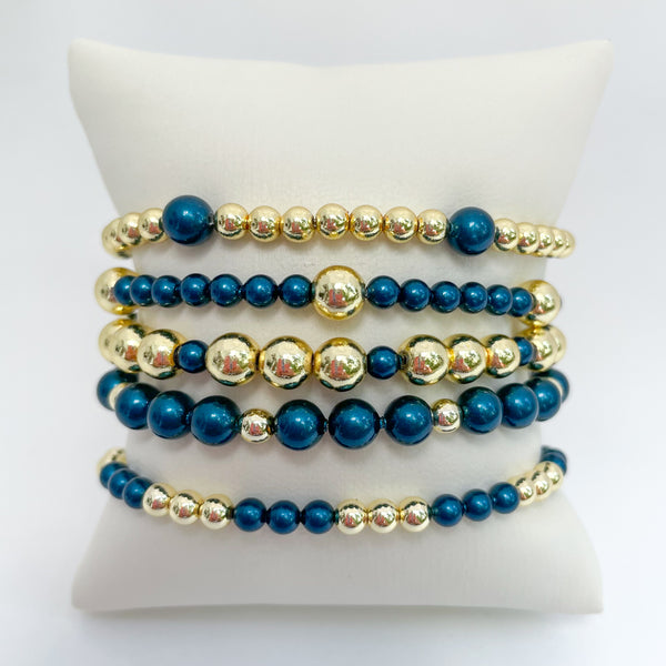 Set of peacock blue austrian crystal pearls and gold beaded bracelets on a white display.