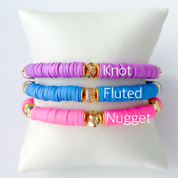 Three colorful bracelets labeled 'Knot', 'Fluted', and 'Nugget' on a white cushion.
