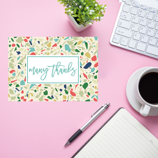 Colorful card with 'many thanks' on a pink desk with a keyboard, pen, and coffee.