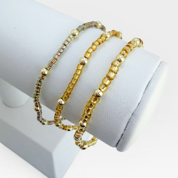 Three gold beaded bracelets on a white stand