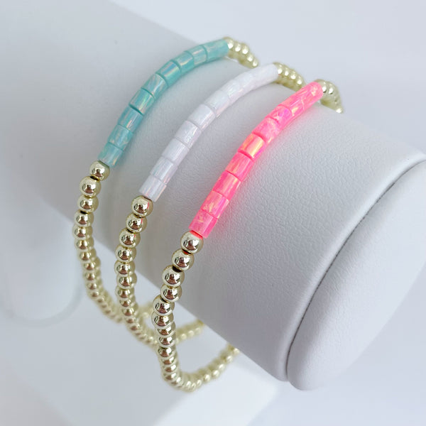 Three opal beaded bracelets in turquoise, white, and pink on a white surface.