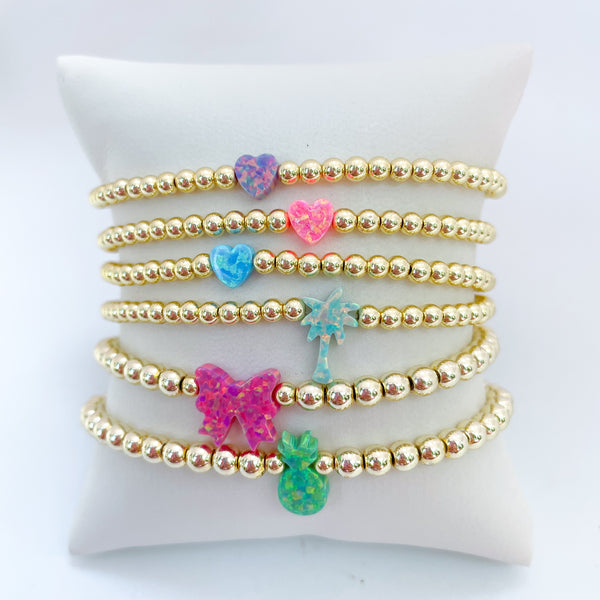 Gold beaded bracelets with colorful opal bow, palm tree, pineapple and heart charms on a white background