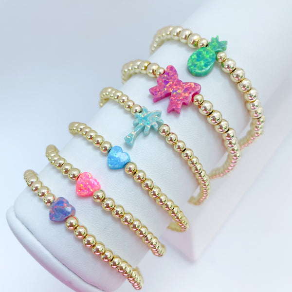 Gold beaded bracelets with colorful opal bow, palm tree, pineapple and heart charms on a white background