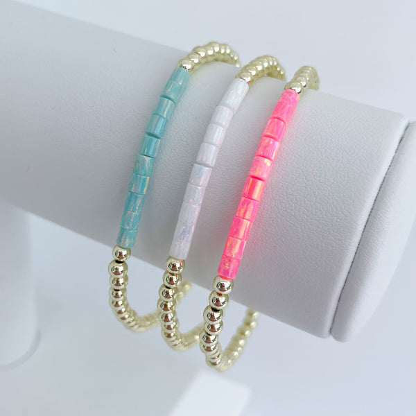 Three opal beaded bracelets in turquoise, white, and pink on a white surface.