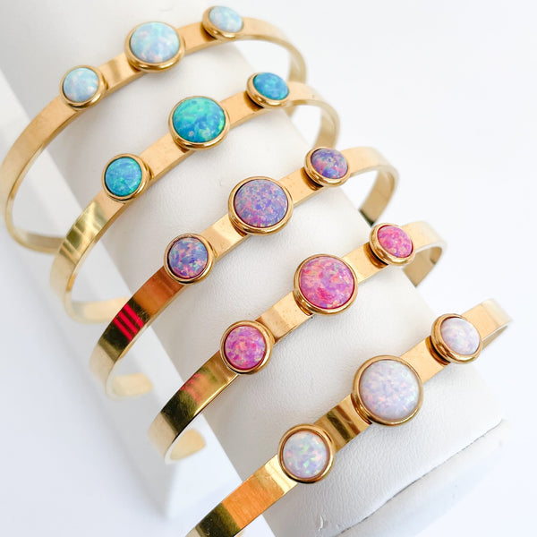 Gold bracelets with colorful opals on a white stand
