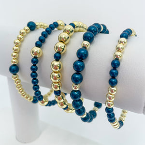 Set of peacock blue austrian crystal pearls and gold beaded bracelets on a white display.
