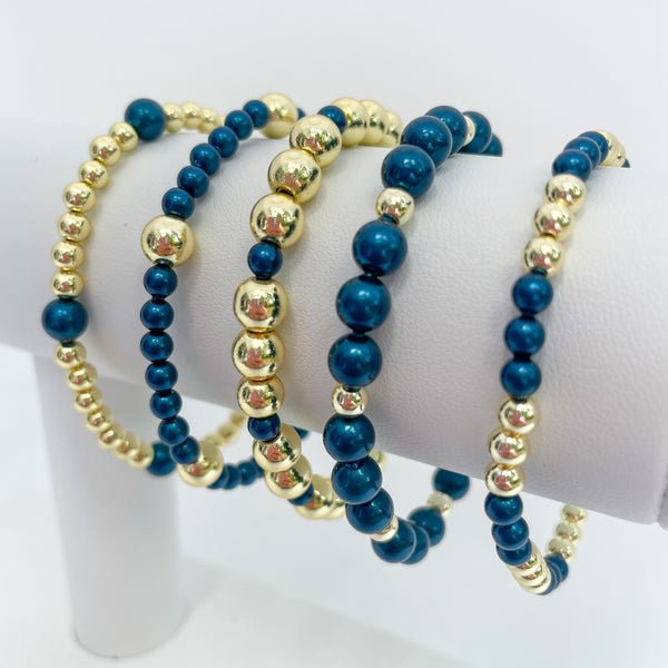 Set of peacock blue austrian crystal pearls and gold beaded bracelets on a white display.