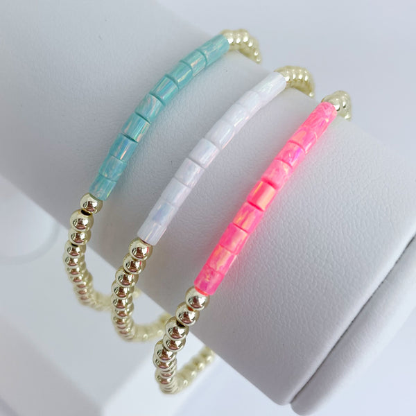 Three opal beaded bracelets in turquoise, white, and pink on a white surface.