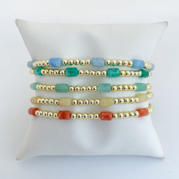 Set of blue, green, yellow and orange colored beaded dyed jade bracelets on a bracelet pillow 