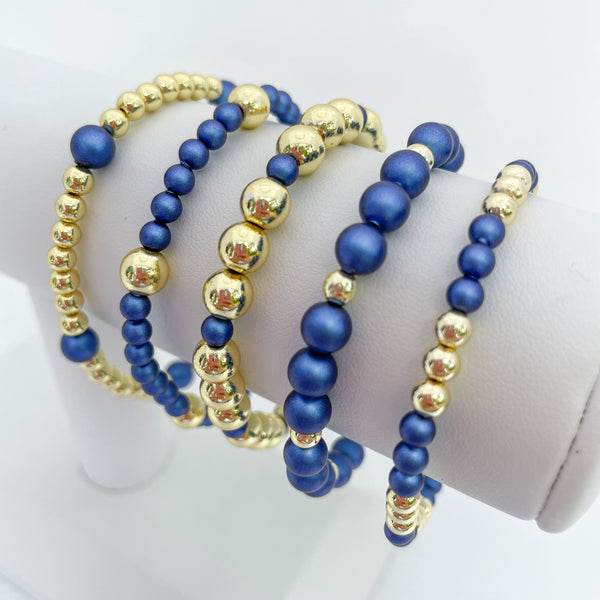 Set of sapphire blue austrian crystal pearls and gold beaded bracelets on a white display.
