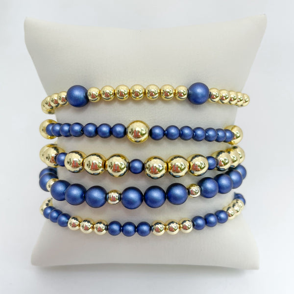 Set of sapphire blue austrian crystal pearls and gold beaded bracelets on a white display.