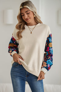 Woman wearing a cream sweater with colorful sleeves and blue jeans indoors.