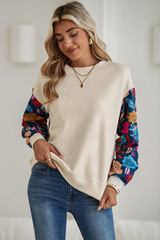 Woman wearing a cream sweater with colorful sleeves and blue jeans indoors.