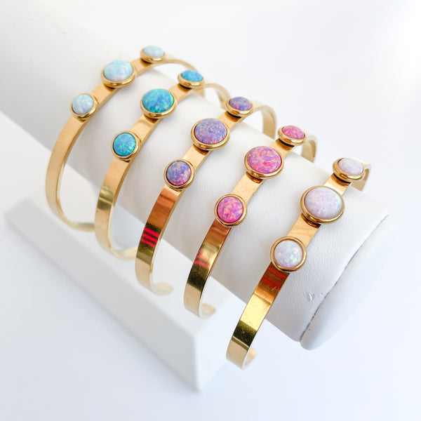 Set of gold bangles with colorful gemstones on a white surface