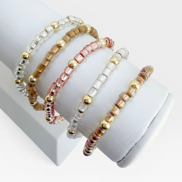 Set of gold, rose gold and silver beaded bracelets on a white surface