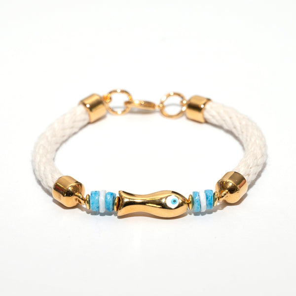 A white braided cord bracelet with gold-tone metal accents, including a central gold fish-shaped charm with a blue evil eye detail, flanked by small blue and white beads and gold cylindrical spacers.