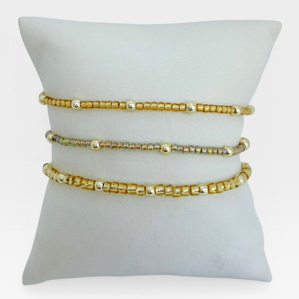 Three gold beaded bracelets on a white cushion