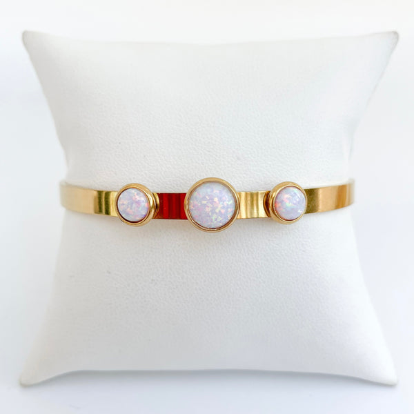 Gold bracelet with three circular opal stones on a white cushion