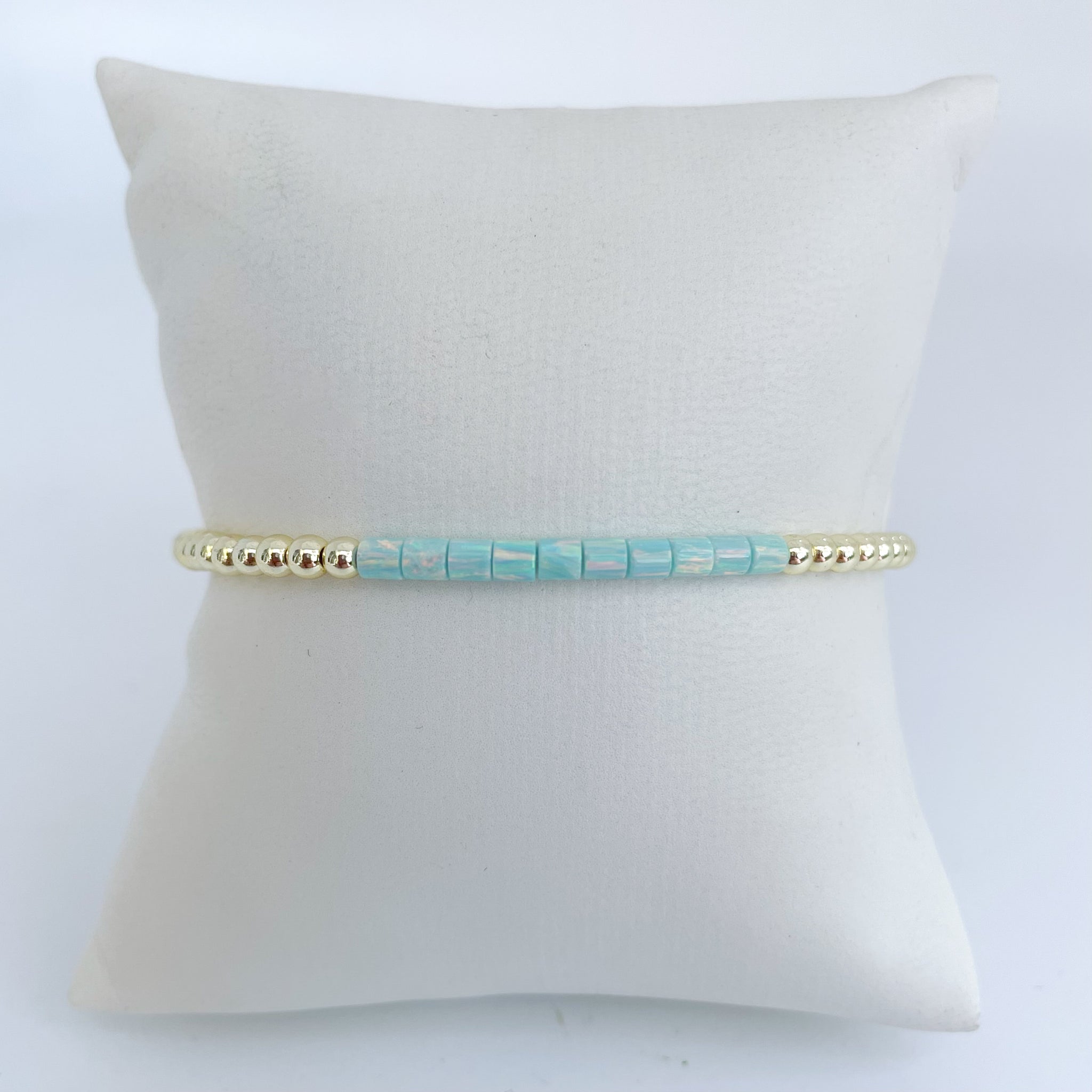 Turquoise opal beaded bracelet with gold accents on a white pillow