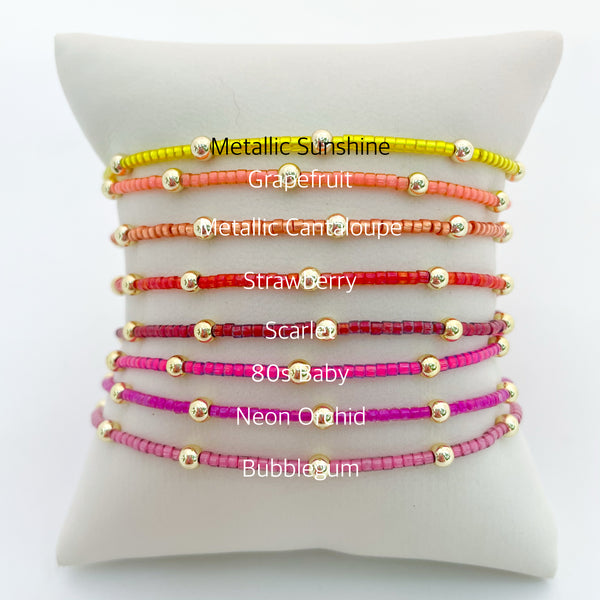 Set of colorful beaded bracelets on a white cushion with color names.