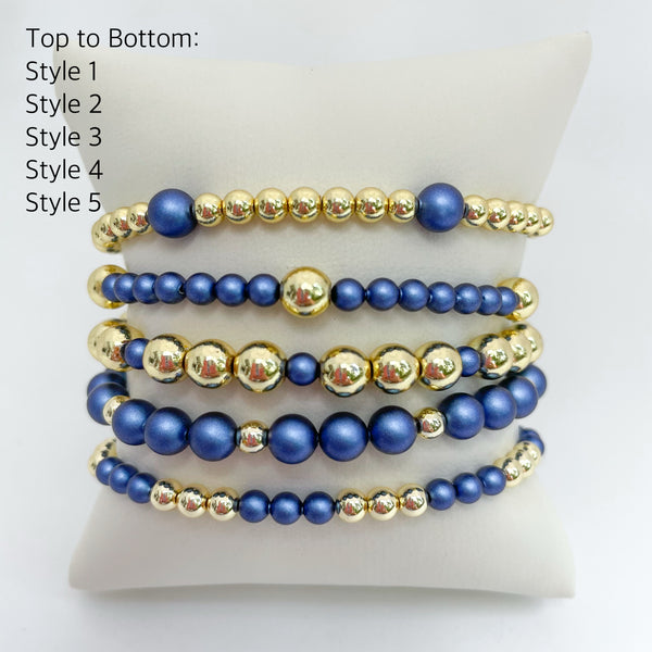 Set of sapphire blue austrian crystal pearls and gold beaded bracelets on a white display.
