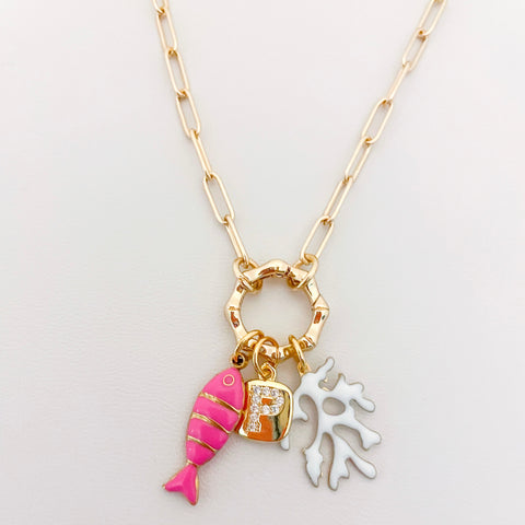 Necklace with pink fish charm, gold letter 'P' charm, and white coral charm on a light gray background