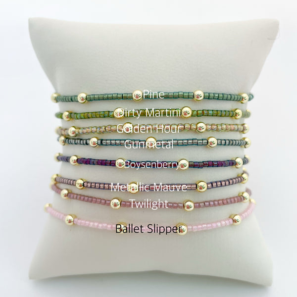 Set of beaded bracelets on a white cushion with color names below each bracelet.