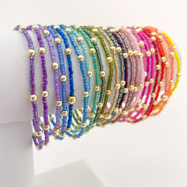 Set of colorful beaded bracelets with gold beads on a white surface