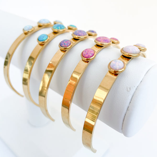 Set of gold bangles with multicolored stones on a white stand