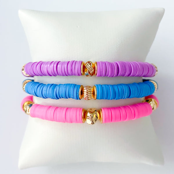 Three colorful bracelets stacked on a white cushion with a white background