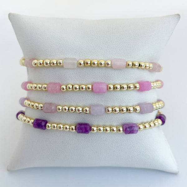 Set of pink and purple colored beaded dyed jade bracelets on a bracelet pillow