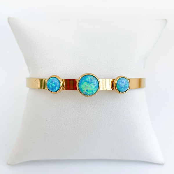 Gold bracelet with three blue gemstones on a white pillow