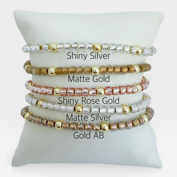 Set of beaded bracelets in various colors on a white cushion with color labels.
