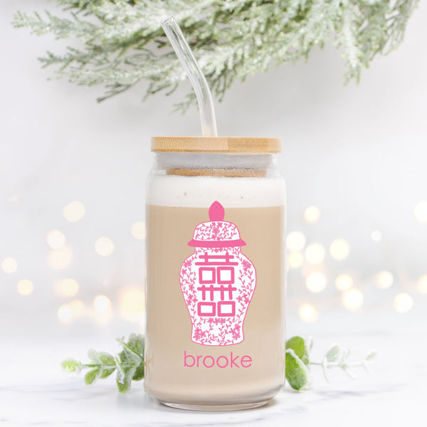 Glass drinking jar with pink ginger jar design and 'brooke' text, against a blurred background with lights and greenery.
