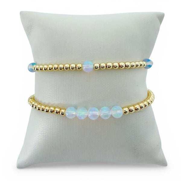 Two beaded opal bracelets on a white cushion with a white background