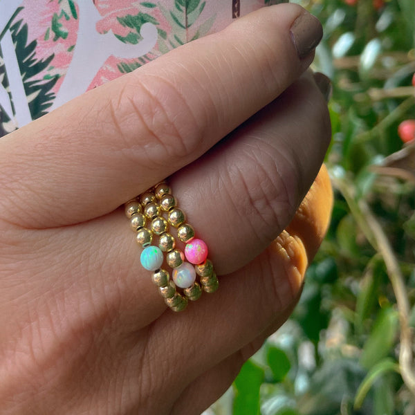 Hand wearing a gold opal ring with colorful beads, holding a pink tumbler.