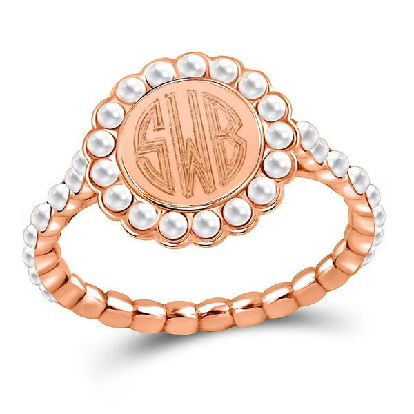 A rose gold signet ring featuring a circular face with a monogrammed 'SWB' center, surrounded by a border of white faux pearls, and a textured rose gold band, shown on a white background.