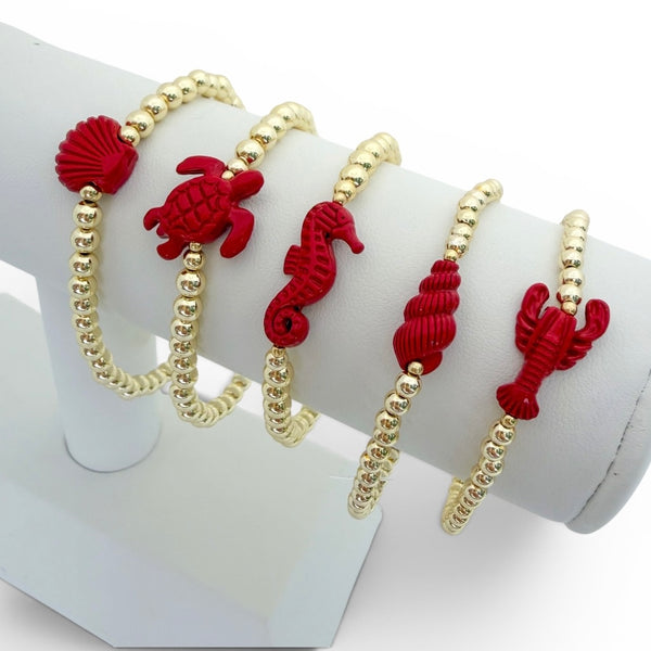 Set of red and gold bracelets with sea creature designs on a white stand.