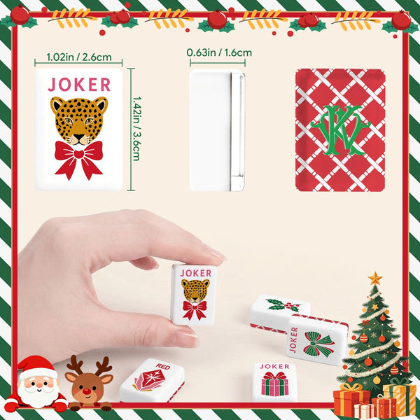 Christmas-themed monogrammed mahjong tiles featuring 'JOKER' designs with a leopard and red bow, plus red patterned back tiles, shown with a hand holding a tile and dimension labels on a festive beige background.