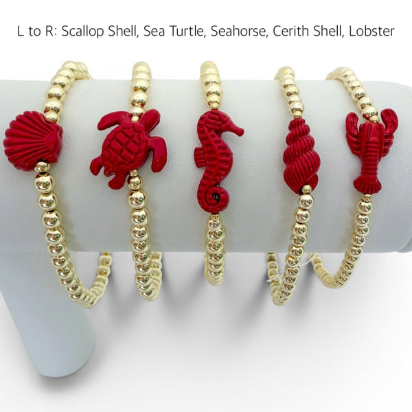 Set of red and gold bracelets with sea creature designs on a white stand.